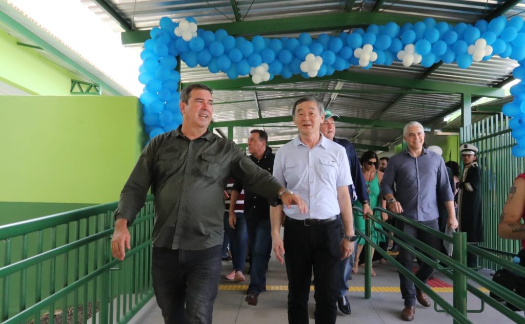 Governador de camisa verde anda na escola ao lado do prefeito de camisa azul clara. Atrás deles balões enfeitam a escola recém inaugurada