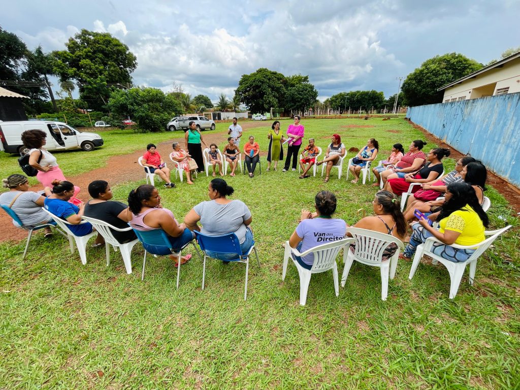 Mulheres estão sentadas em círculo no gramado do evento discutindo temas sobre o cotidiano das mulheres