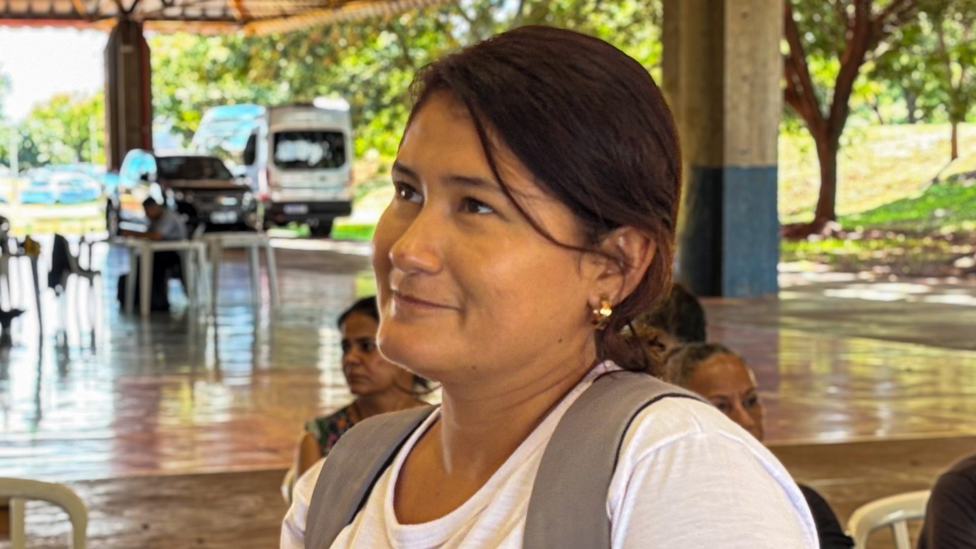 Senhora de camiseta branca, cabelo preso e mochila nas costas.